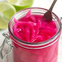 a spoon in a jar filled with pink colored liquid next to sliced limes on a white surface