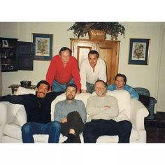 a group of men sitting on top of a white couch in a living room next to each other