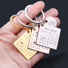 a hand holding three different key chains with calendar charms attached to them, both in gold and silver