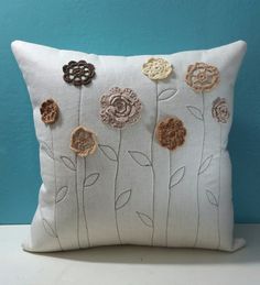 a white pillow with crocheted flowers on the front and back, sitting against a blue wall