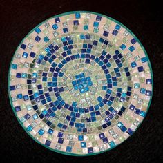 a blue and green mosaic tile design on a black table top in the shape of a circle