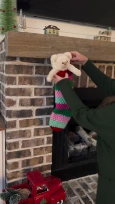 a woman holding a stuffed animal in front of a fire place