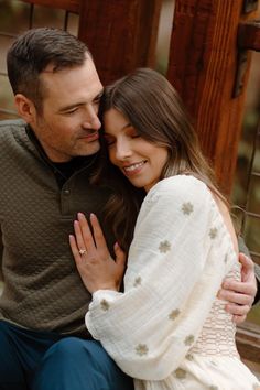 a man and woman sitting next to each other on a wooden bench with their arms around each other