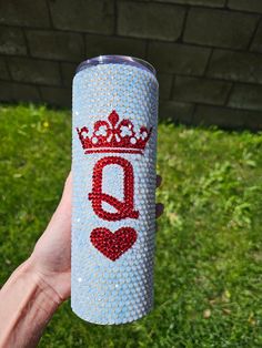 a person holding up a cup with the word q on it and a crown painted on it