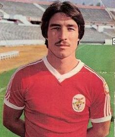 a man standing in front of a soccer field wearing a red shirt and white shorts