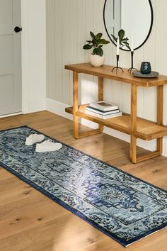 a blue rug on the floor in front of a wooden table with a mirror and plant