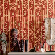 a shelf with books and vases on it in front of a wallpapered background