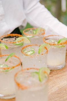 several glasses filled with drinks sitting on top of a wooden table next to each other