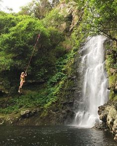 a woman hanging from a rope near a waterfall