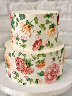 a three tiered cake decorated with flowers and leaves on a white plate next to a brick wall