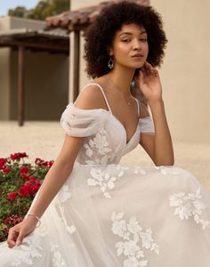 a woman in a white wedding dress sitting on the ground next to some red flowers