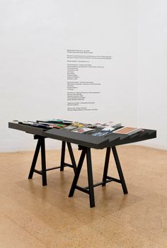 a black table with magazines on it in front of a white wall and wooden floor