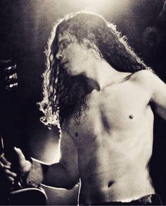 a shirtless man with long hair and no shirt holding a guitar in his right hand