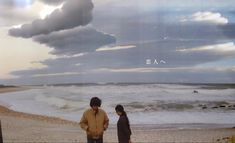 two people are standing on the beach looking at the water and clouds in the sky