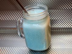 a glass jar filled with blue liquid sitting on top of a metal tile floor next to a spoon