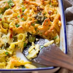 a casserole dish with noodles and vegetables in it on a cloth next to a wooden spoon