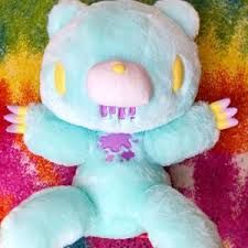 a blue stuffed animal with yellow eyes sitting on a rainbow colored surface and holding it's arms out