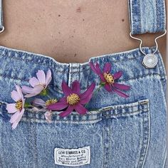 a woman's stomach with flowers in the back pocket of her jean overalls