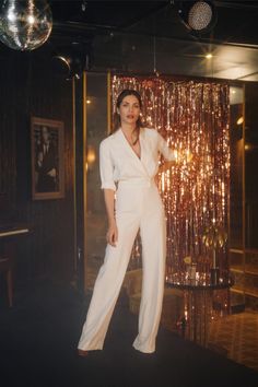 a woman standing in front of a disco ball backdrop wearing a white suit and heels