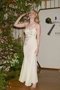 a woman in a white dress standing next to a wall with pink flowers on it