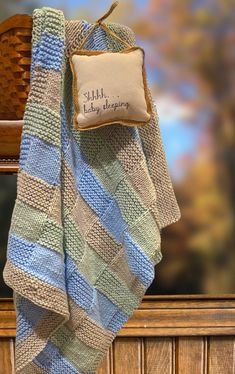 a blue and green striped blanket sitting on top of a wooden bench next to a pillow