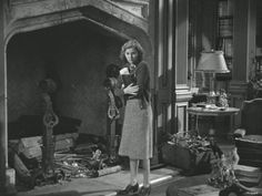 an old photo of a woman standing in front of a fireplace