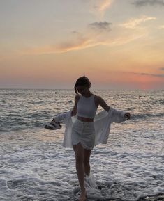 a woman standing on top of a sandy beach next to the ocean at sunset or dawn