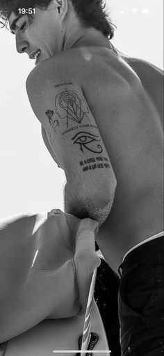 a man with a tattoo on his arm holding a surfboard