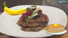 a stack of pancakes topped with fruit on top of a white plate next to a banana