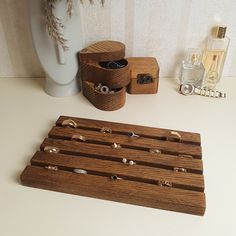 a wooden rack with rings on it next to a white vase and other jewelry items