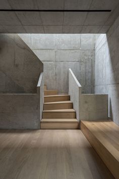 an empty concrete room with stairs leading up to the second floor and light wood floors