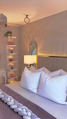 a large bed with white pillows in a bedroom next to a chandelier and mirror