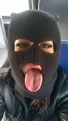 a woman sticking her tongue out while wearing a black knitted hat and mask on top of her head