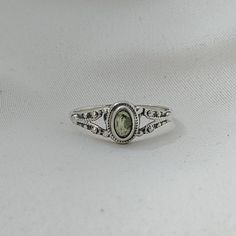 a silver ring with a green stone in the center on a white cloth covered surface