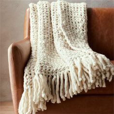 a white knitted blanket sitting on top of a brown leather couch next to a wall