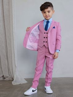 a young boy in a pink suit and tie holding a white jacket over his shoulder