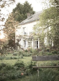 an old house with a wooden bench in the foreground, and trees surrounding it