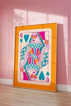 a pink and orange framed playing card on a wooden floor in front of a pink wall