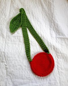 a crocheted red and green object laying on top of a white bed sheet