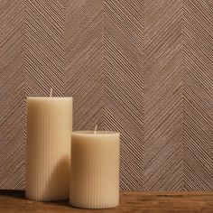 two white candles sitting next to each other on top of a wooden table in front of a wall