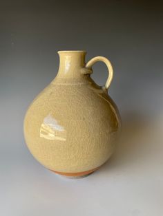 a large yellow vase sitting on top of a white table next to a gray wall