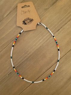 a white beaded bracelet with multi colored beads on a wooden table next to a tag