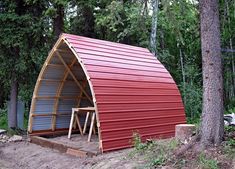 a red metal building sitting in the middle of a forest next to a tall tree