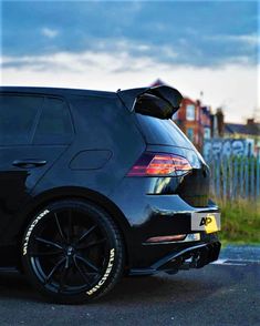 the back end of a black car parked in a parking lot next to a fence