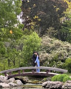 two people standing on a bridge over a pond