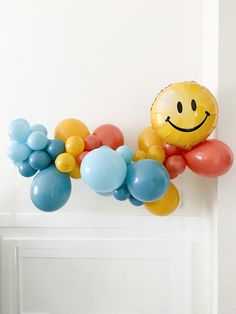 a bunch of balloons are hanging on the wall with a smiley face balloon attached to it