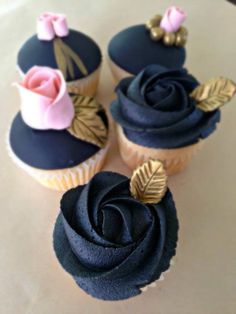 three cupcakes decorated with black frosting and gold leaf decorations on a table