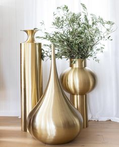 three gold vases sitting on top of a wooden floor next to a planter