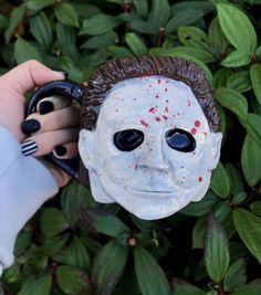 a person holding a fake mask in front of some bushes and plants with their hands