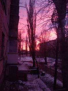 the sun is setting behind some trees and snow on the ground in front of an apartment building
